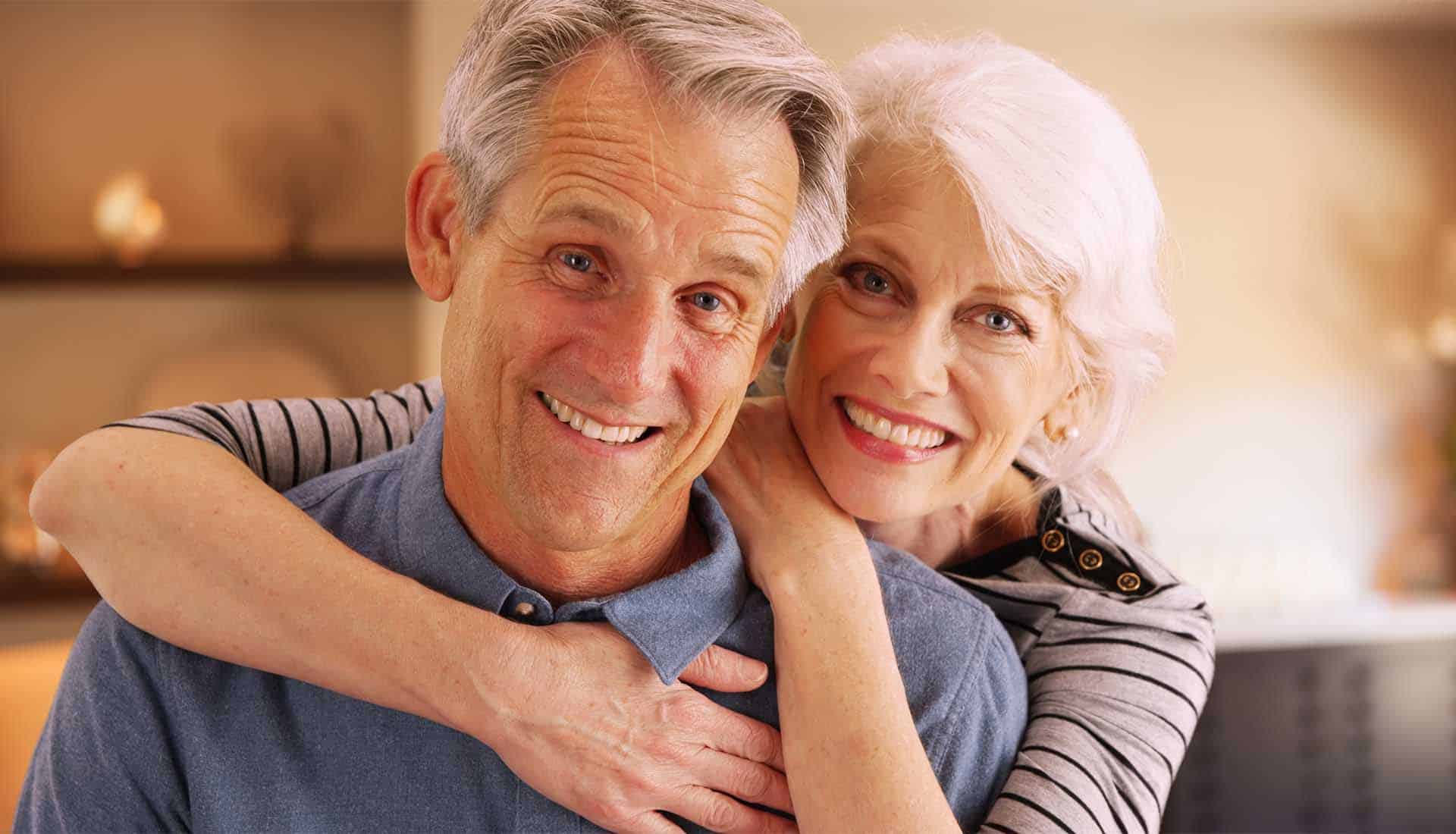 Happy elderly couple sitting at home smiling.